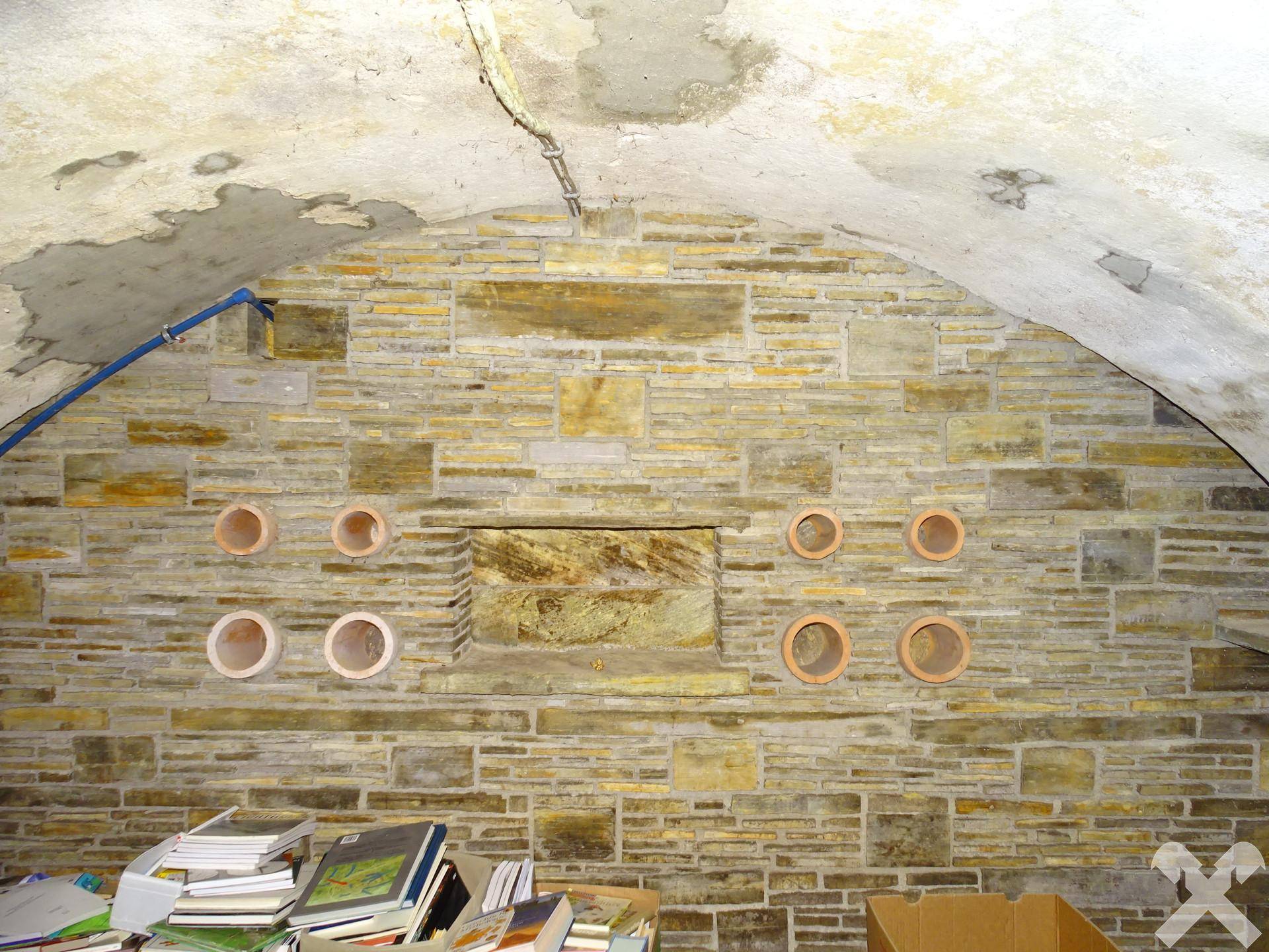Detailansicht der Natursteinwand im Gewölbekeller mit dekorativen runden Öffnungen.