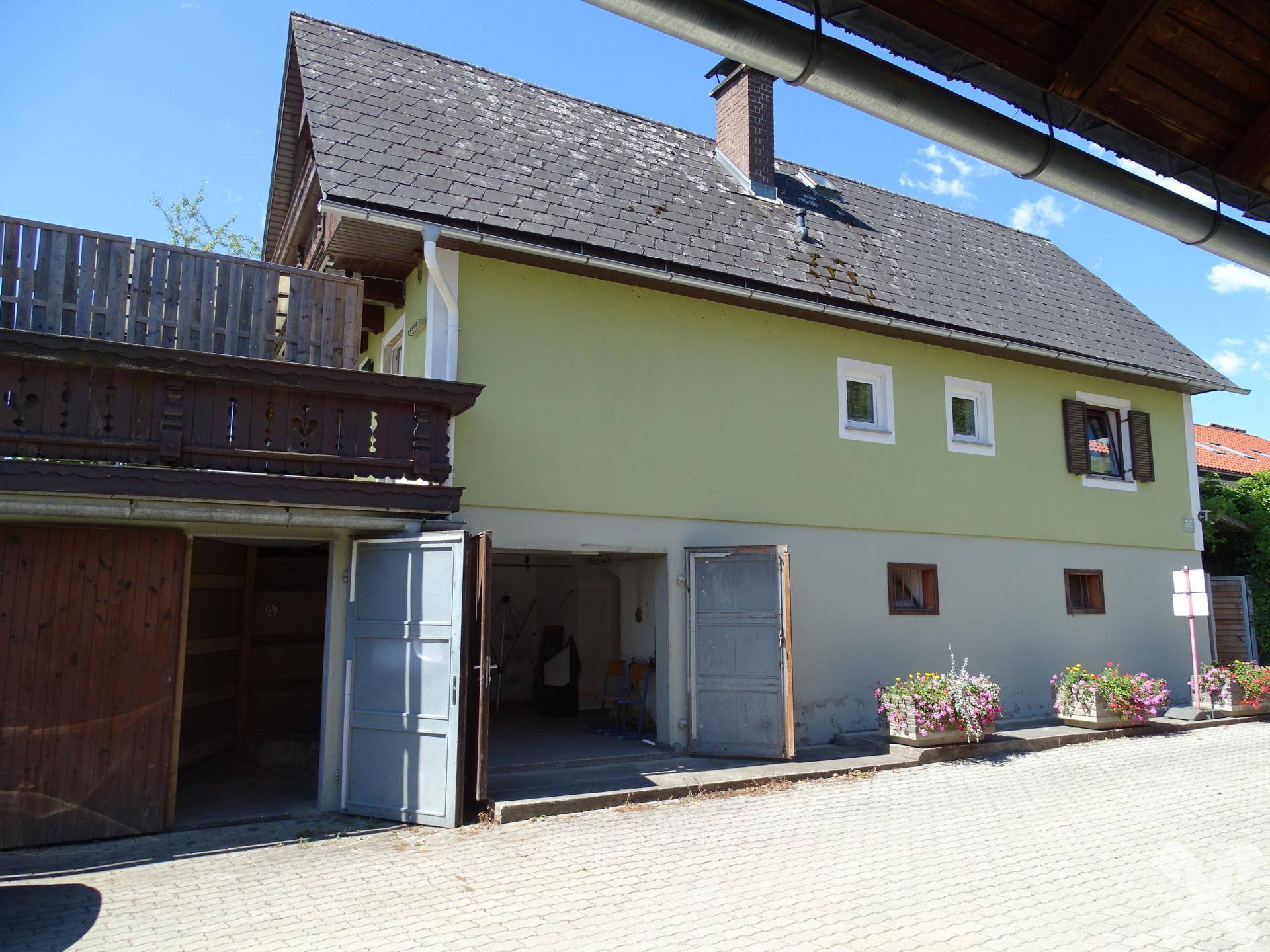 Seitenansicht des Hauses mit Garagentoren und einem Balkon im oberen Bereich.