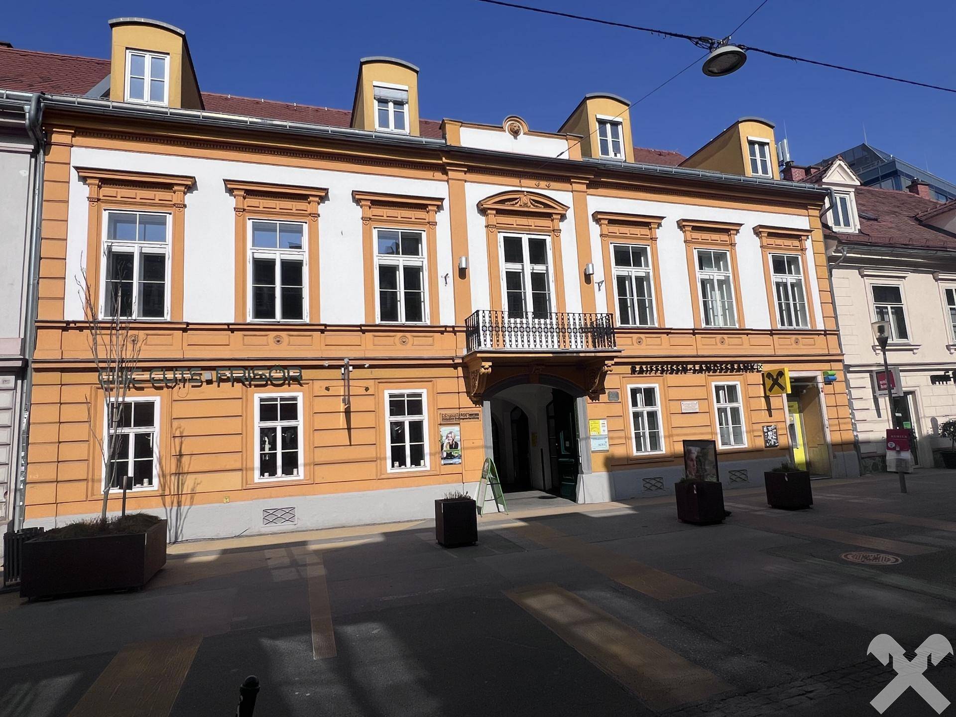 Historisches Gebäude mit orangefarbener Fassade, weißen Fenstern und einem dekorativen Balkon in der Stadt.
