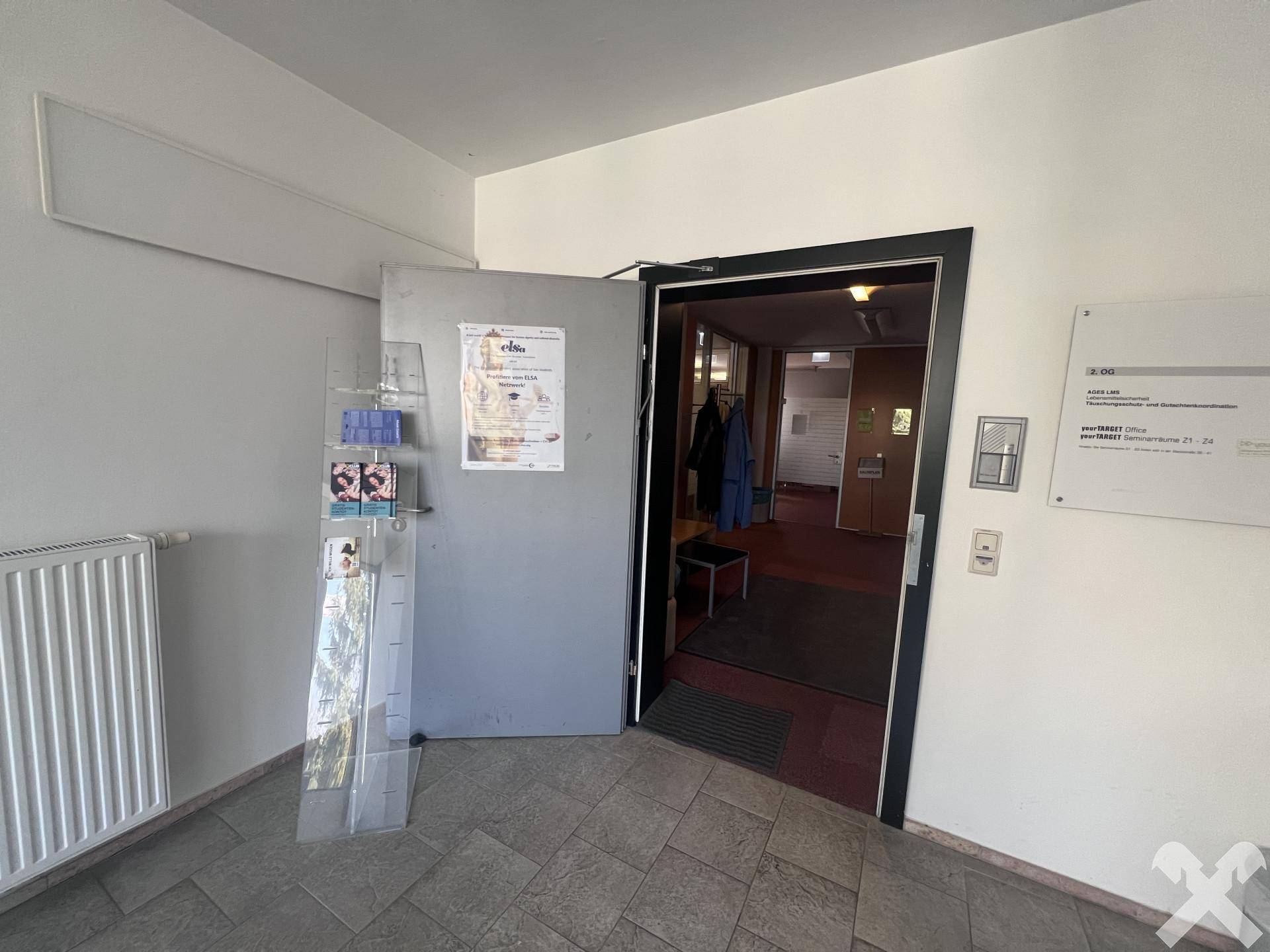 Eingang zu einem Büro oder Geschäftsbereich mit Heizkörper und Informationsständer.