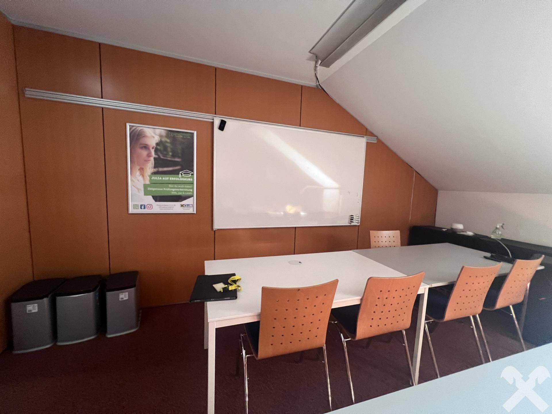Konferenzraum mit schräger Decke, Whiteboard und einem langen Tisch für Besprechungen.