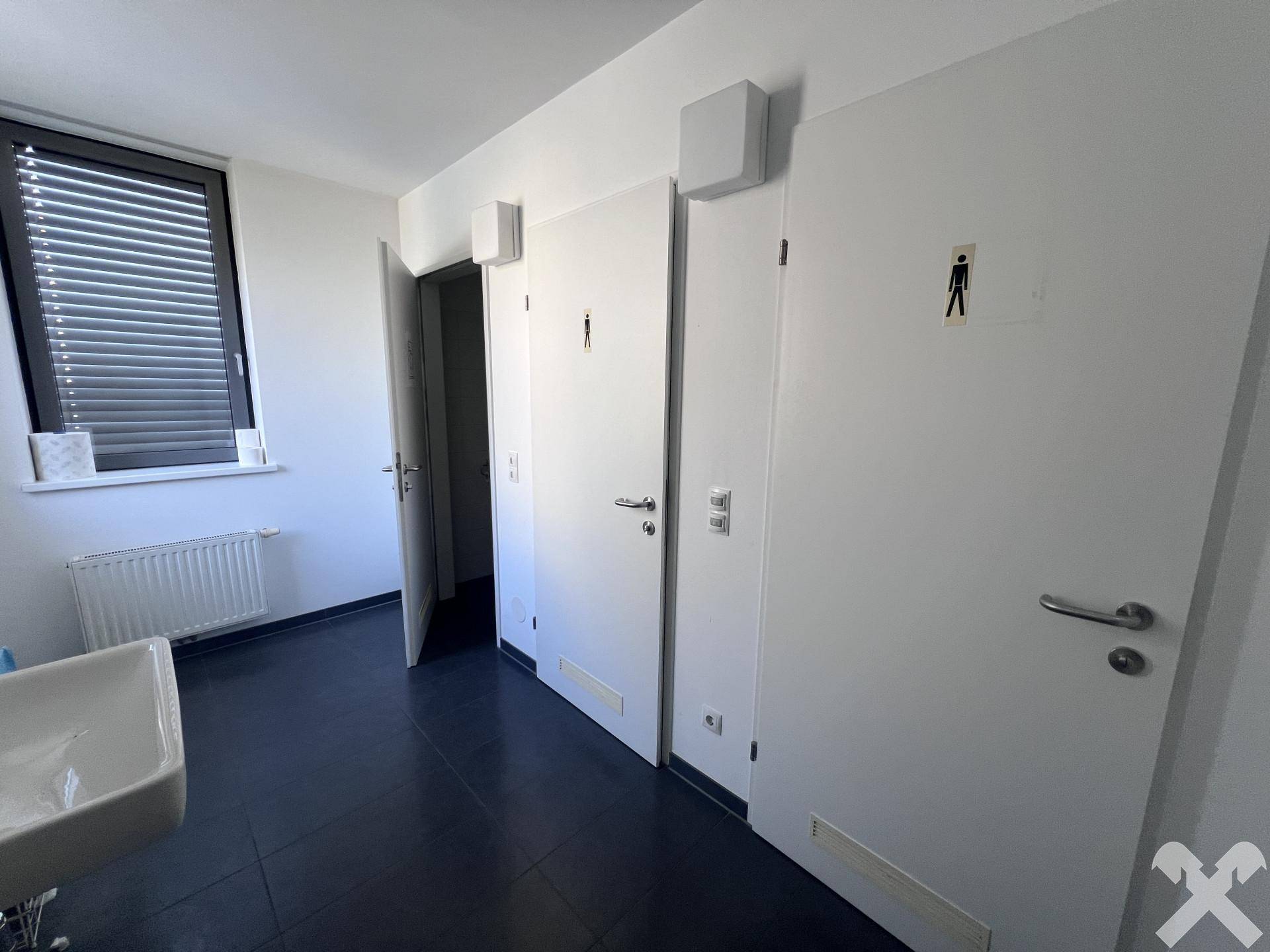 Waschraum mit mehreren Toilettenkabinen und einem Fenster, das für Belüftung sorgt.