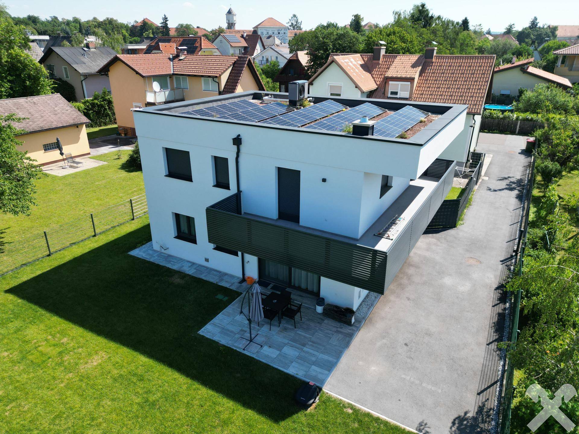 Luftaufnahme des modernen Hauses mit Photovoltaikanlage auf dem Flachdach und umliegender Bebauung.