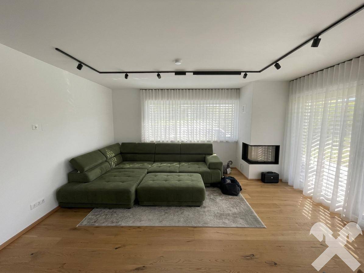Gemütliches Wohnzimmer mit großem Ecksofa, Holzboden, Kamin und viel Tageslicht.