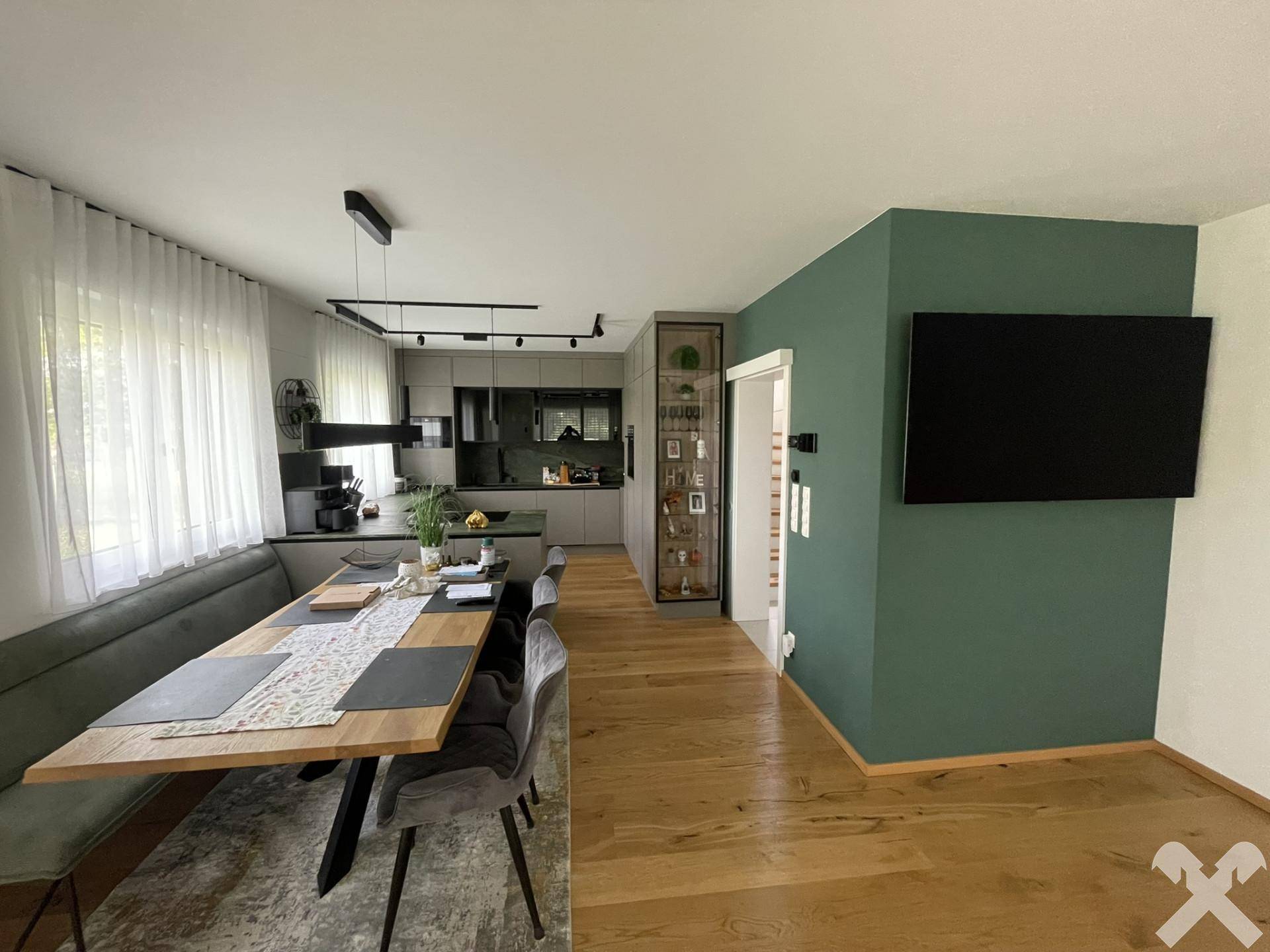 Offener Wohn- und Essbereich mit Holzboden, moderner Küche und grün akzentuierter Wand.