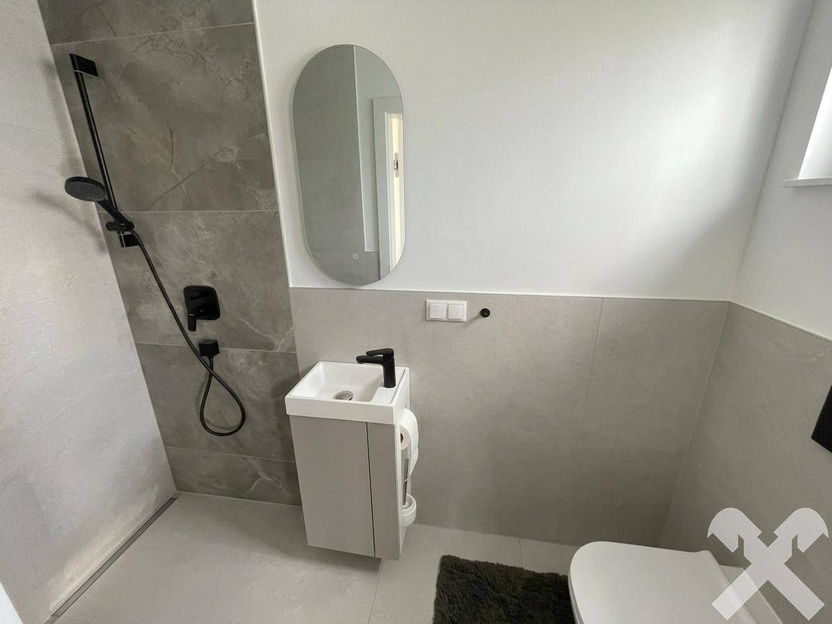 Modernes Badezimmer mit grauen Fliesen, schwarzer Armatur und bodengleicher Dusche.