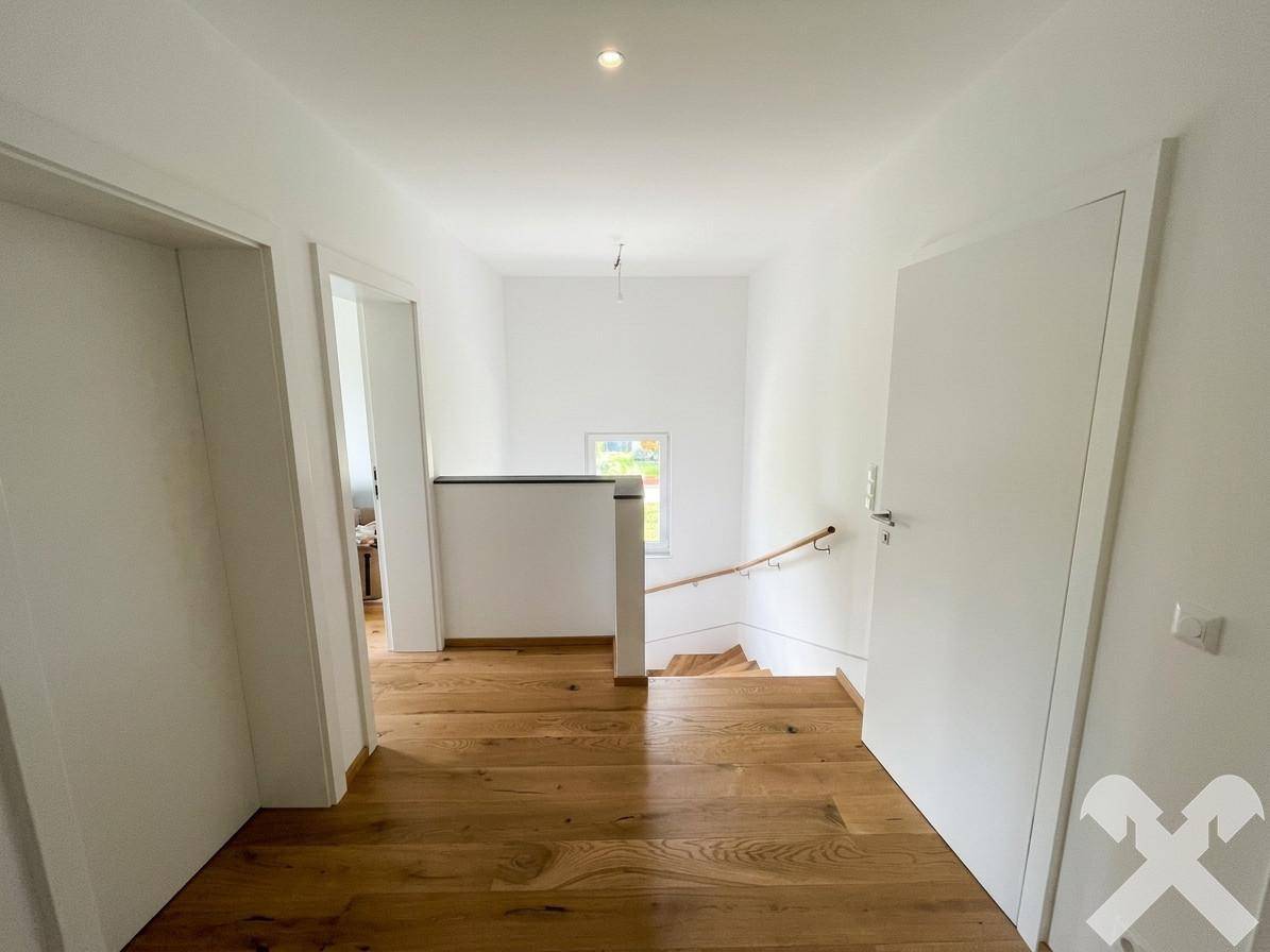 Heller Flur im Obergeschoss mit Holzboden und Treppenaufgang, der viel Tageslicht erhält.