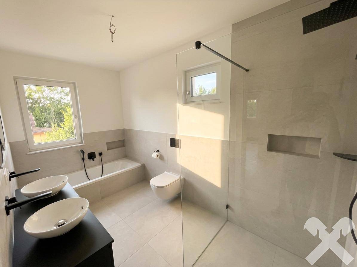 Geräumiges Badezimmer mit Doppelwaschbecken, Badewanne, Dusche und Fenster für Tageslicht.
