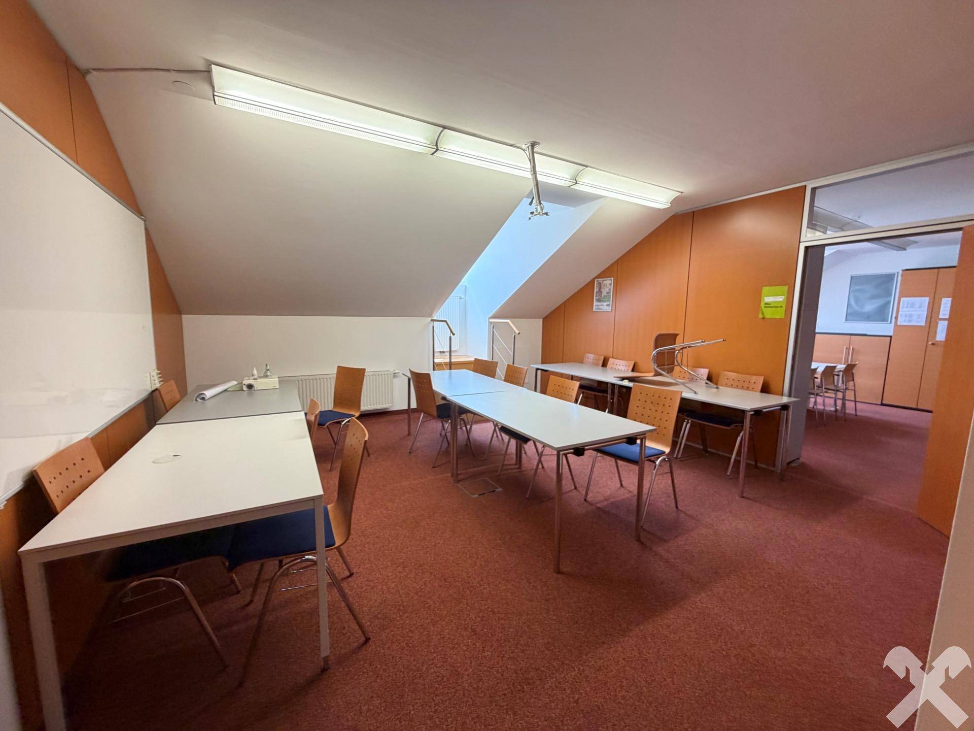 Geräumiger Schulungsraum mit Teppichboden, schräger Decke und Zugang zu weiteren Räumen.