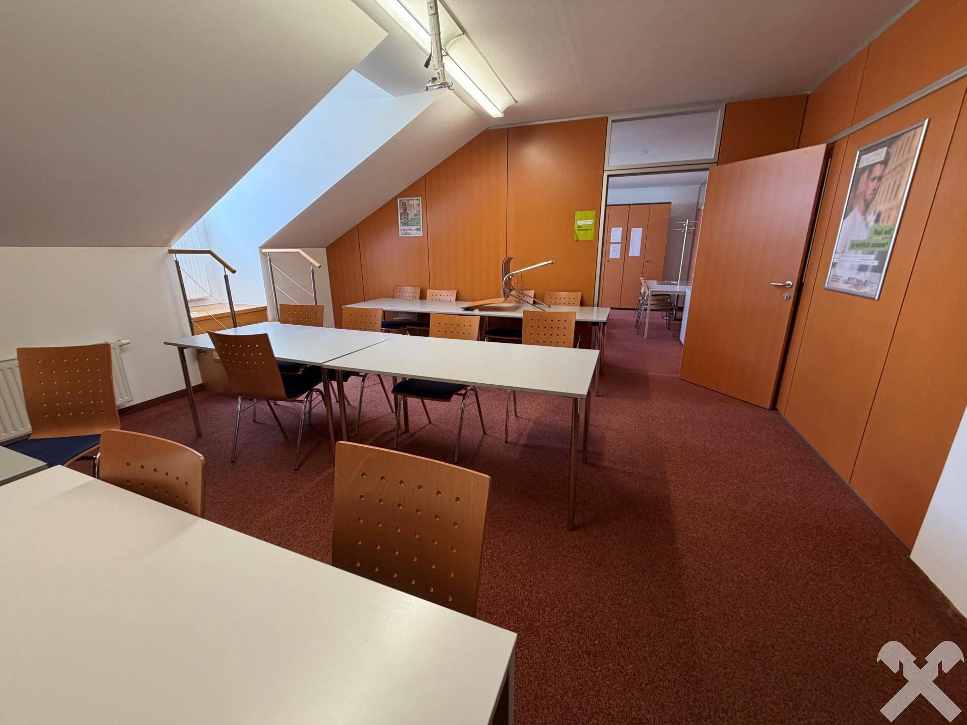 Schulungsraum mit Tischen, Stühlen und einer schrägen Decke, die den Dachgeschosscharakter betont.