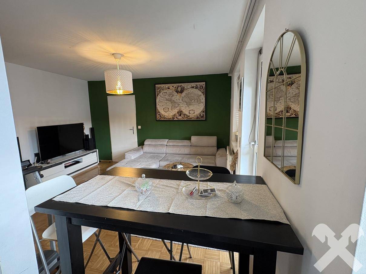 Offener Wohnbereich mit Esstisch im Vordergrund und Blick auf das Sofa und den Fernseher.