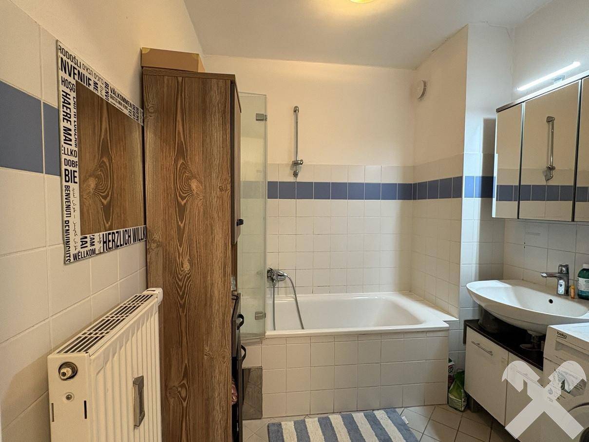 Badezimmer mit Badewanne, Duschfunktion, Waschbecken und Heizkörper, gefliest in Weiß und Blau.