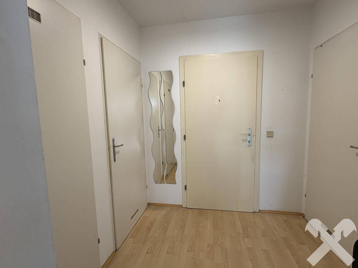 Heller Flur mit Eingangstür, Spiegel und Zugang zu weiteren Räumen, mit Laminatboden.
