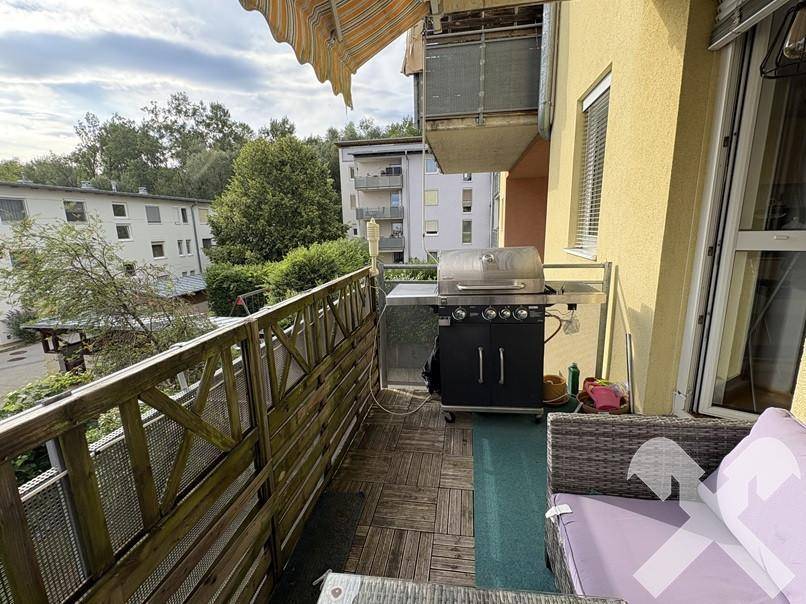 Balkon mit Grillbereich und Sitzgelegenheiten, umgeben von Bäumen und mit Blick ins Grüne.