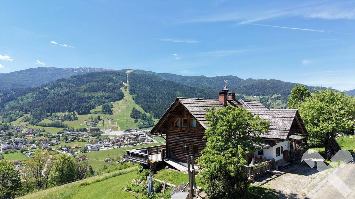 Traditionelles Holzhaus mit Balkon und weitem Blick über ein Tal und bewaldete Berge.