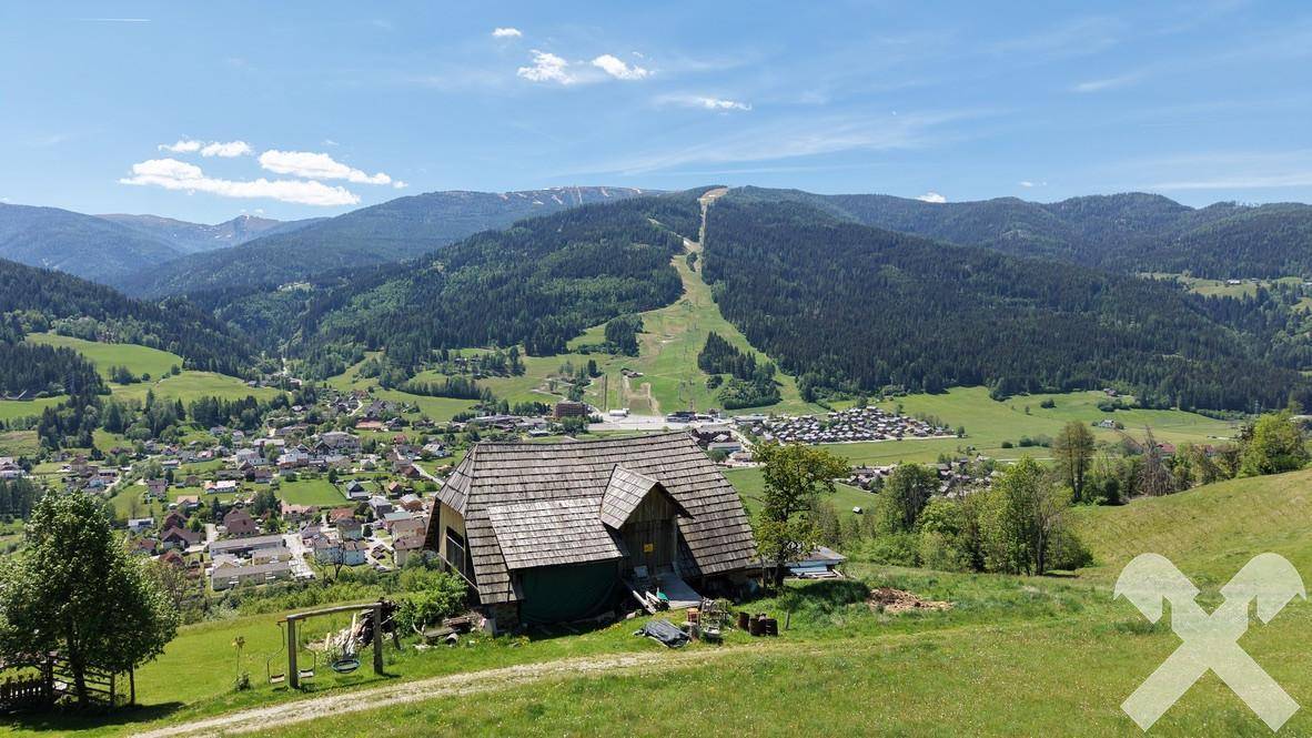 Kleines, rustikales Gebäude mit Holzdach und weitem Blick über ein grünes Tal und Berge.