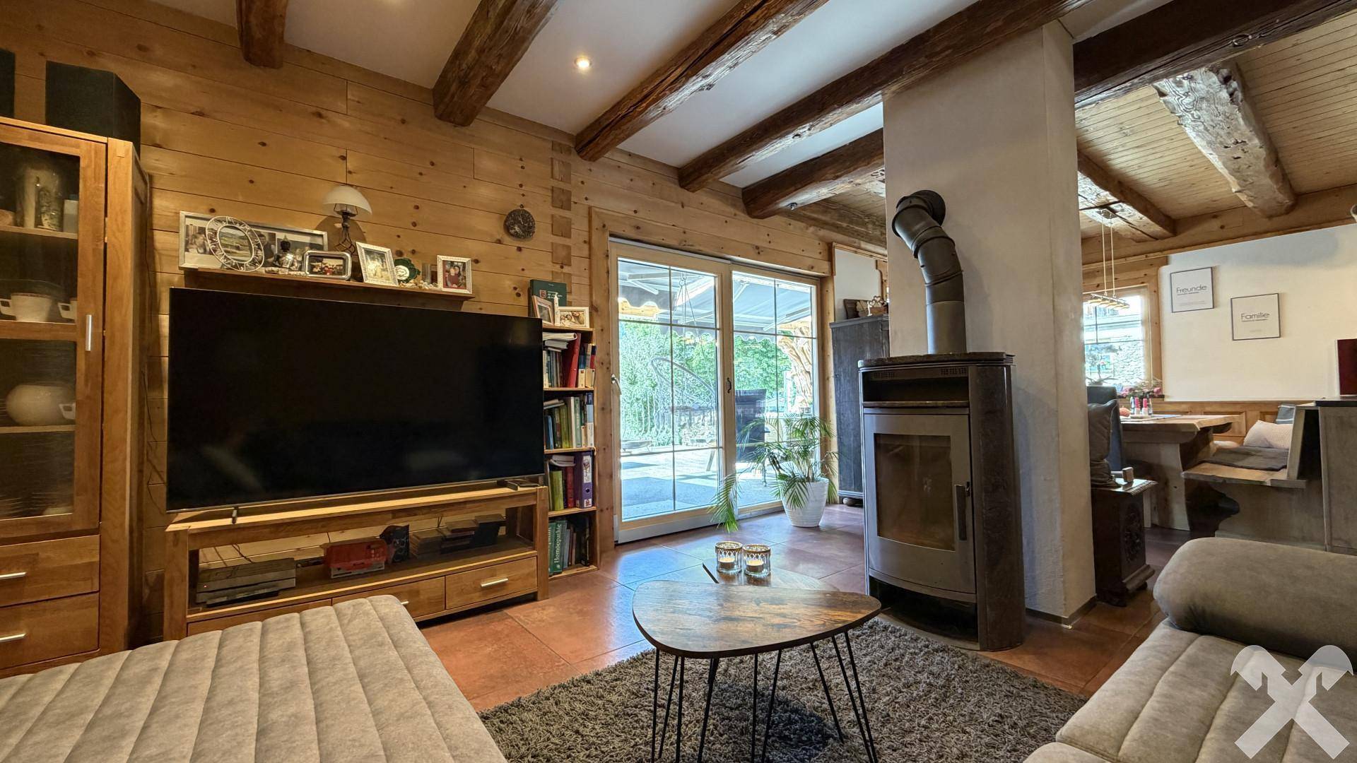 Wohnzimmer mit Holzbalkendecke, Kaminofen und Zugang zu einer Außenterrasse.