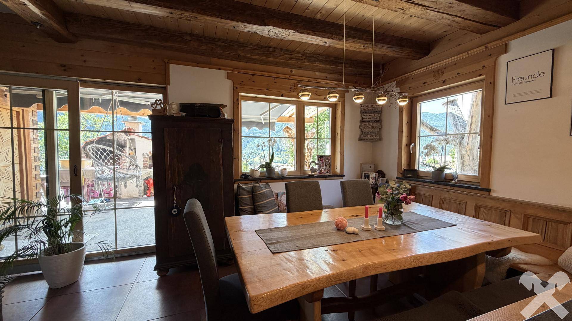 Rustikaler Essbereich mit großem Holztisch, Holzbalkendecke und Zugang zur Terrasse.