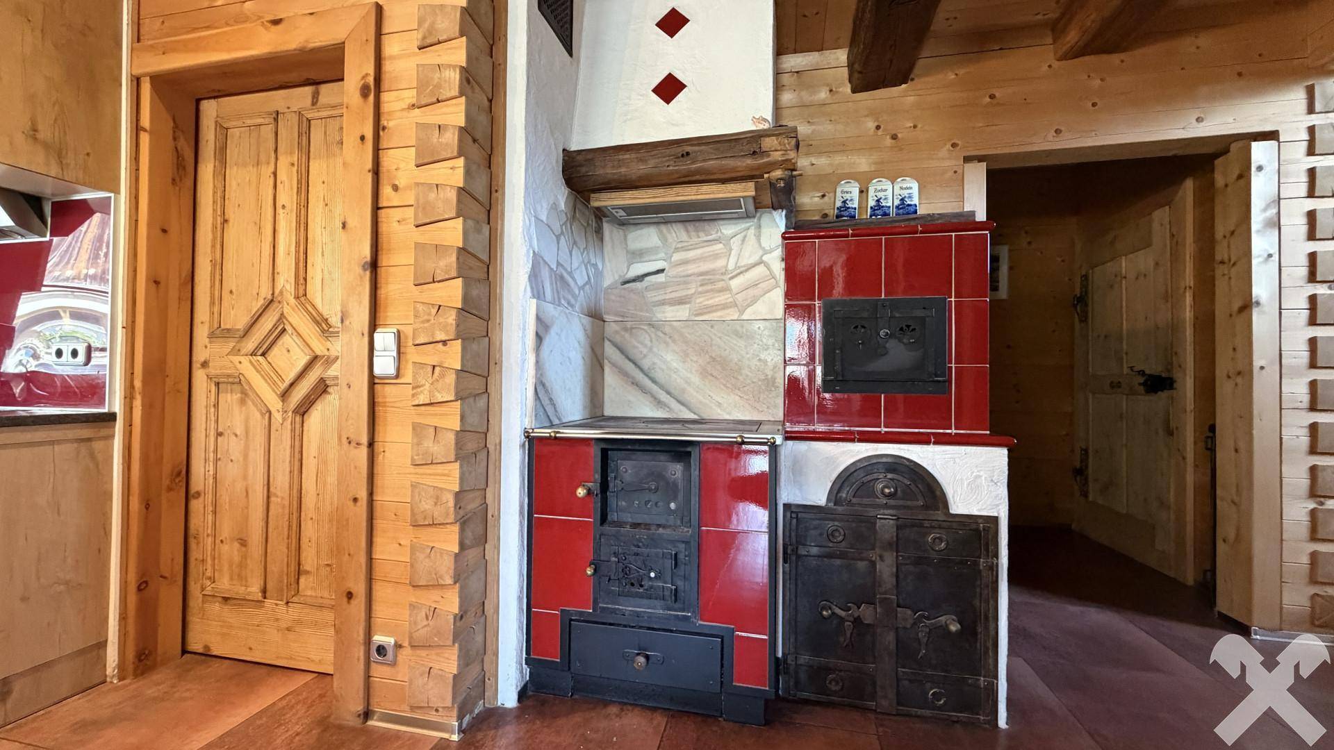 Traditioneller Kachelofen und Holzherd in einer rustikalen Küche mit Holztüren.