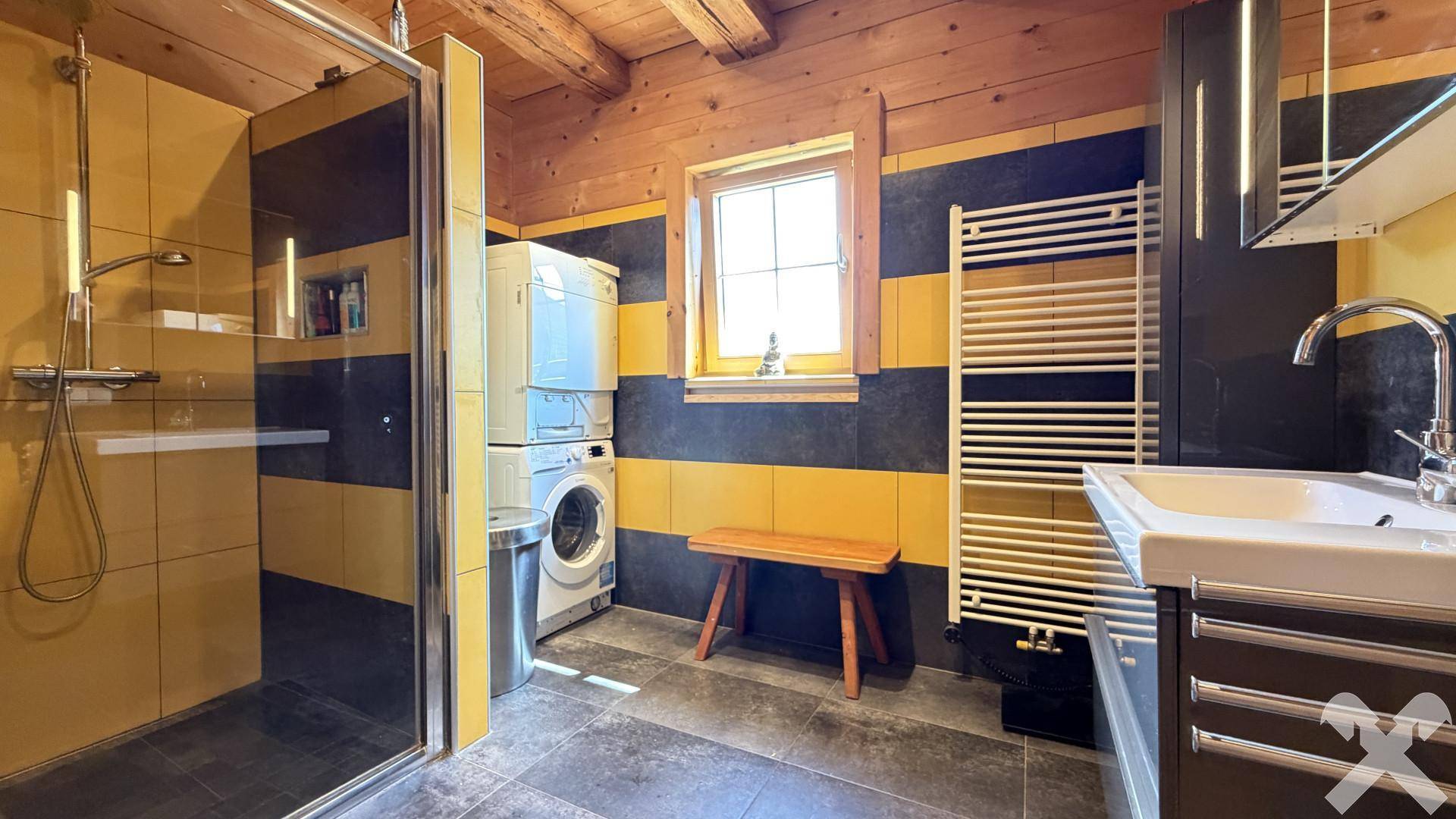 Modernes Badezimmer mit Dusche, Waschmaschine, Trockner und gelb-schwarzen Fliesen.