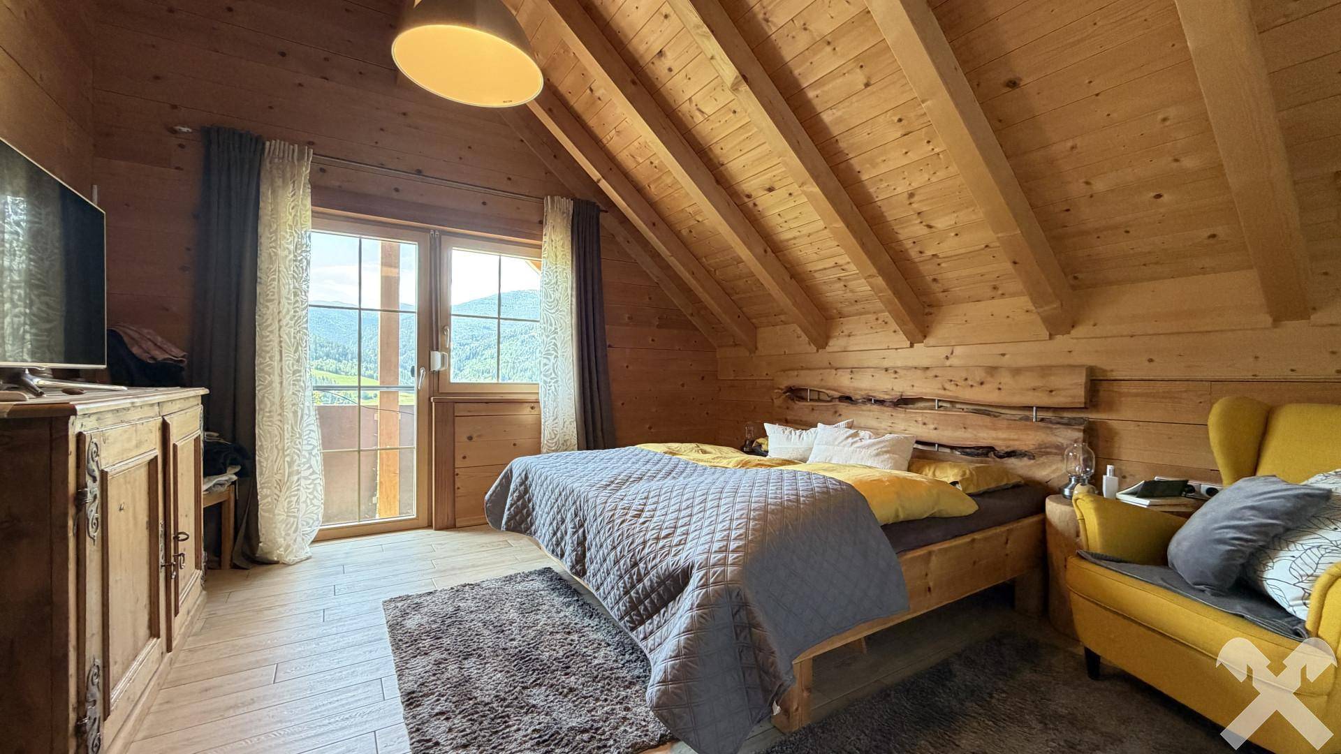 Gemütliches Schlafzimmer mit Holzdachschrägen, Balkonzugang und Bergblick.