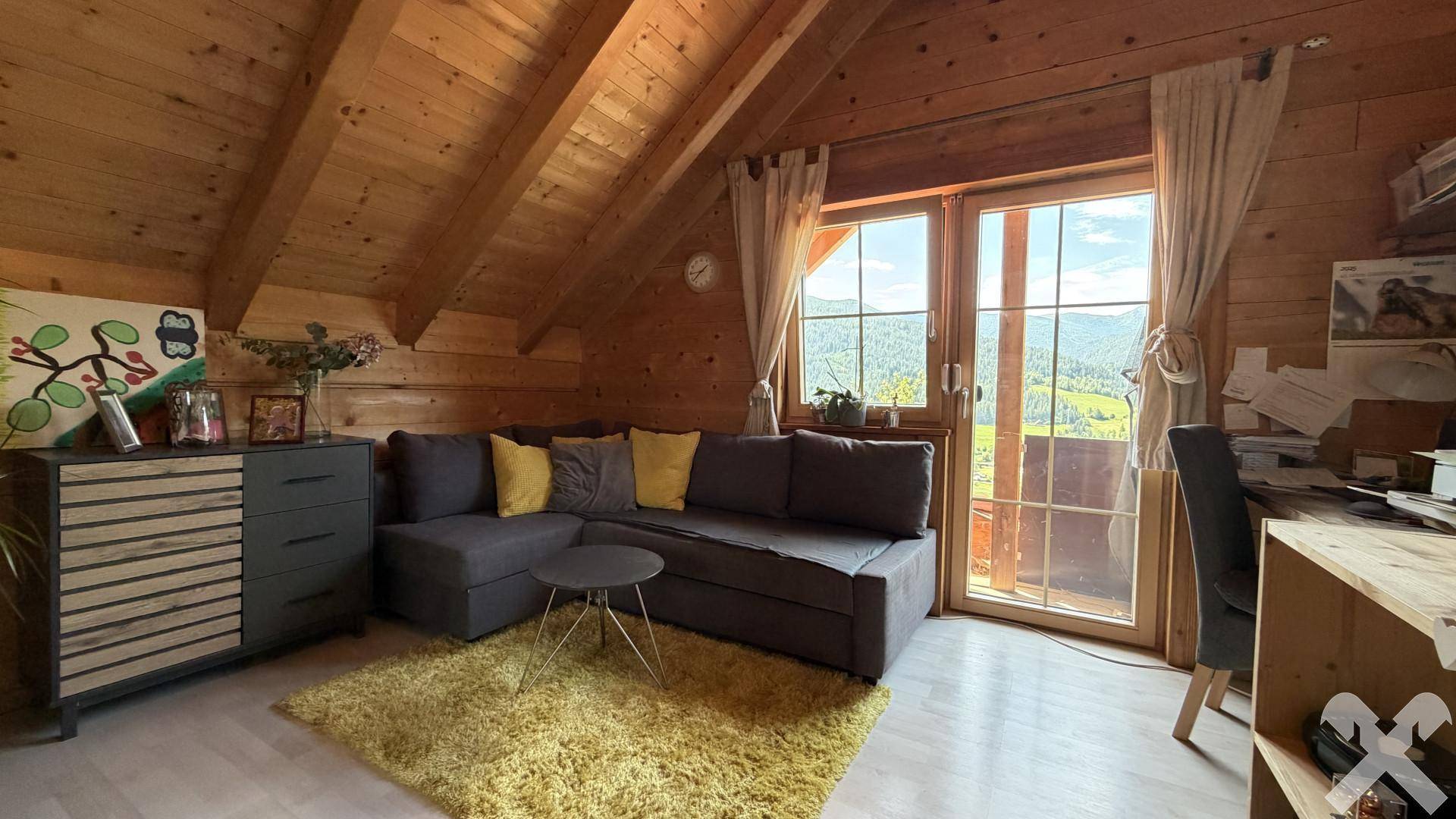 Helles Zimmer mit Holzdachschrägen, Sofa und Schreibtisch, mit Blick auf die Landschaft.