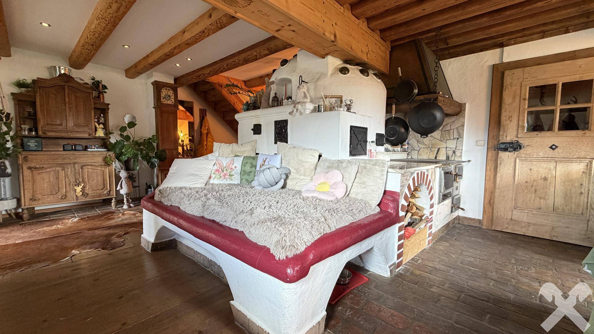 Gemütliches Wohnzimmer mit traditionellem Kachelofen, Holzbalkendecke und rustikalen Möbeln.