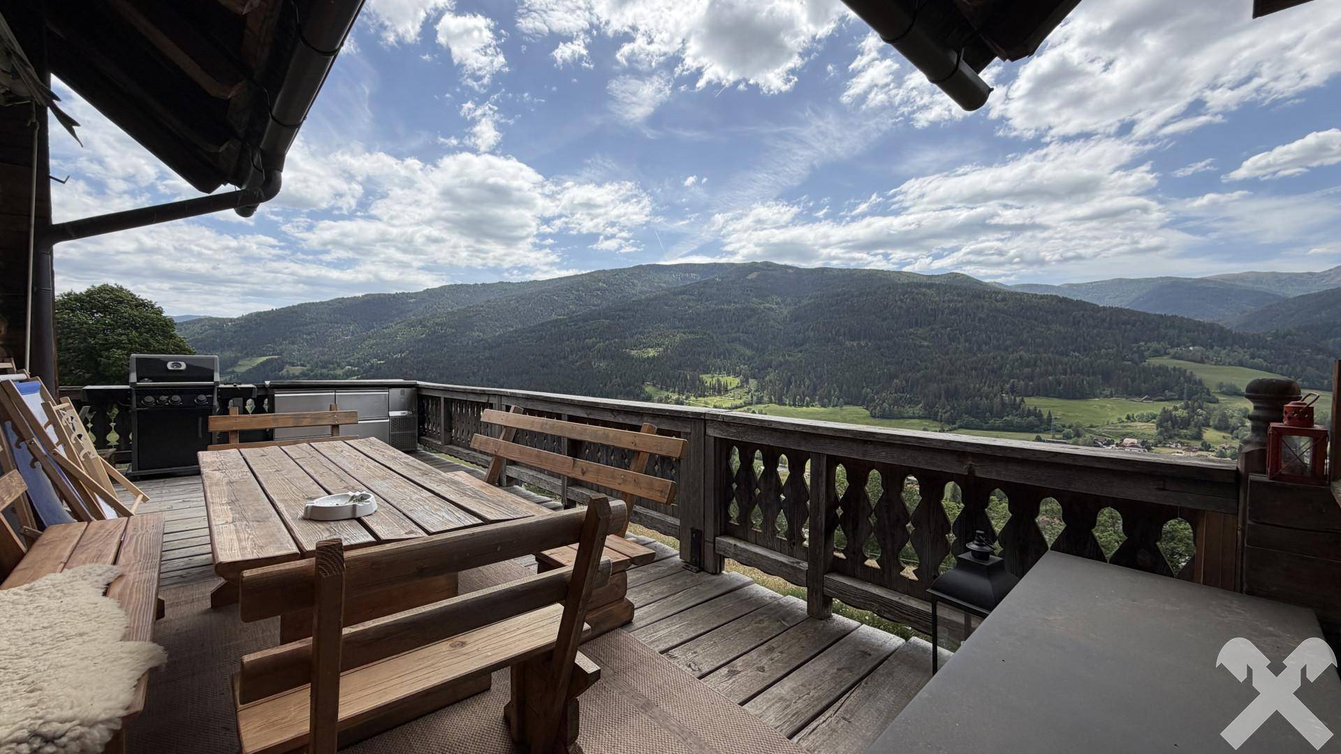 Große Holzterrasse mit Esstisch, Bänken und Panoramablick auf die umliegenden Berge.
