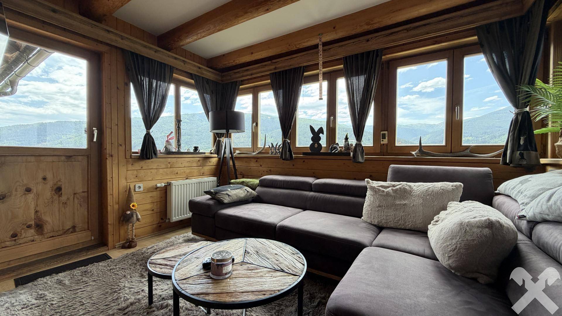 Helles Wohnzimmer mit großen Fenstern, Holzbalkendecke und weitem Bergblick.