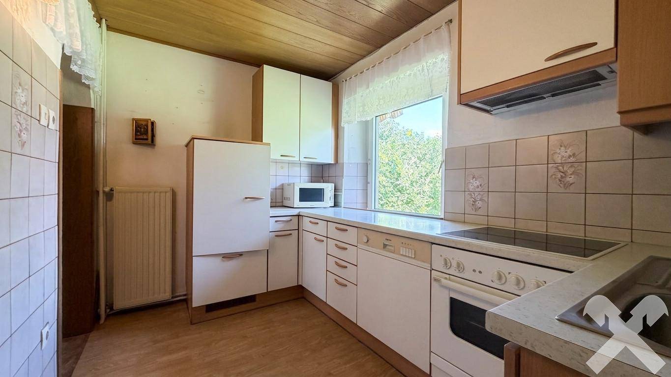 Funktionale Küche mit weißen Einbauschränken, Fliesen und Fenster mit Grünblick.