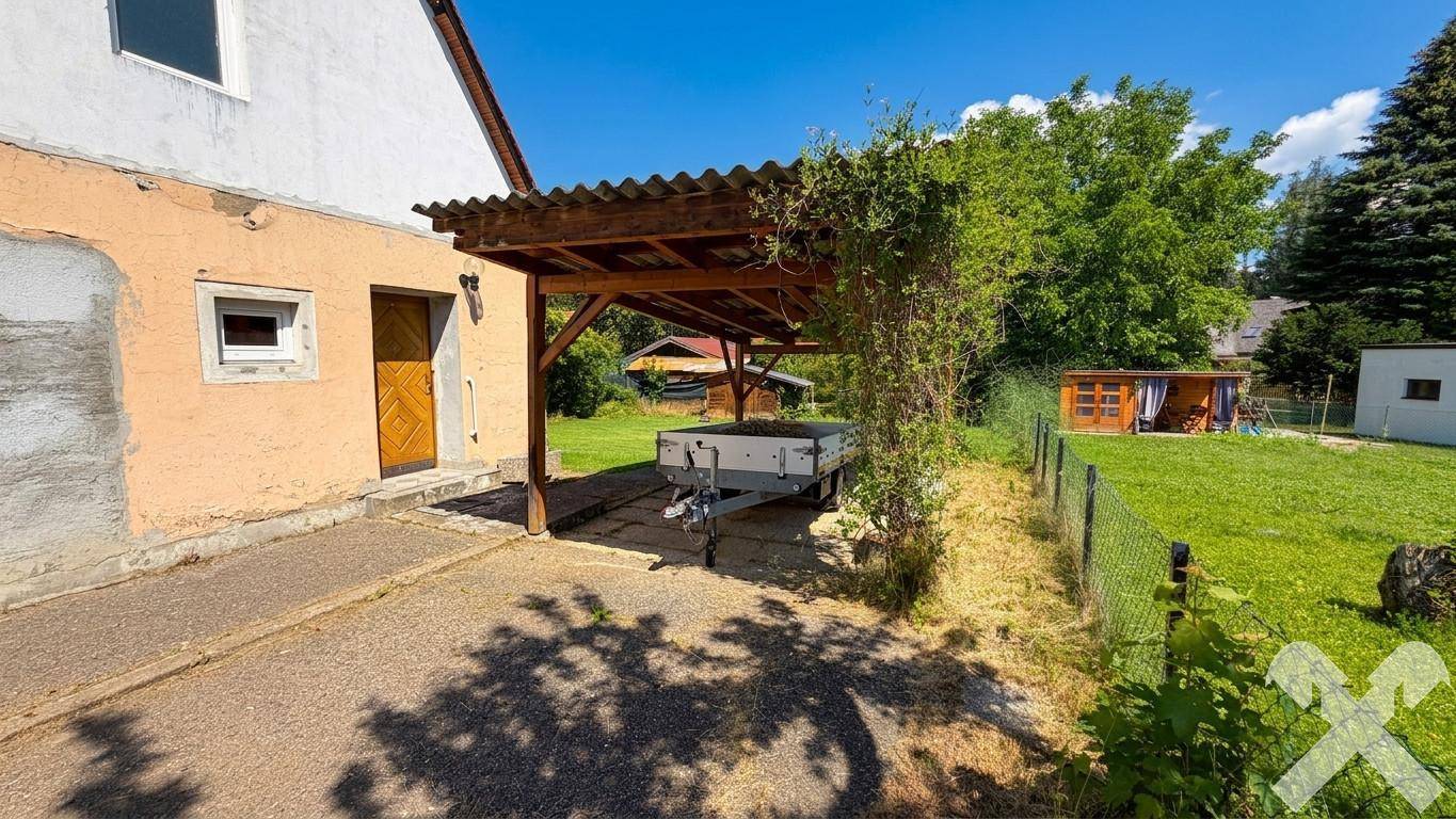 Seitenansicht des Hauses mit Carport, Anhänger und gepflegtem Gartenbereich.