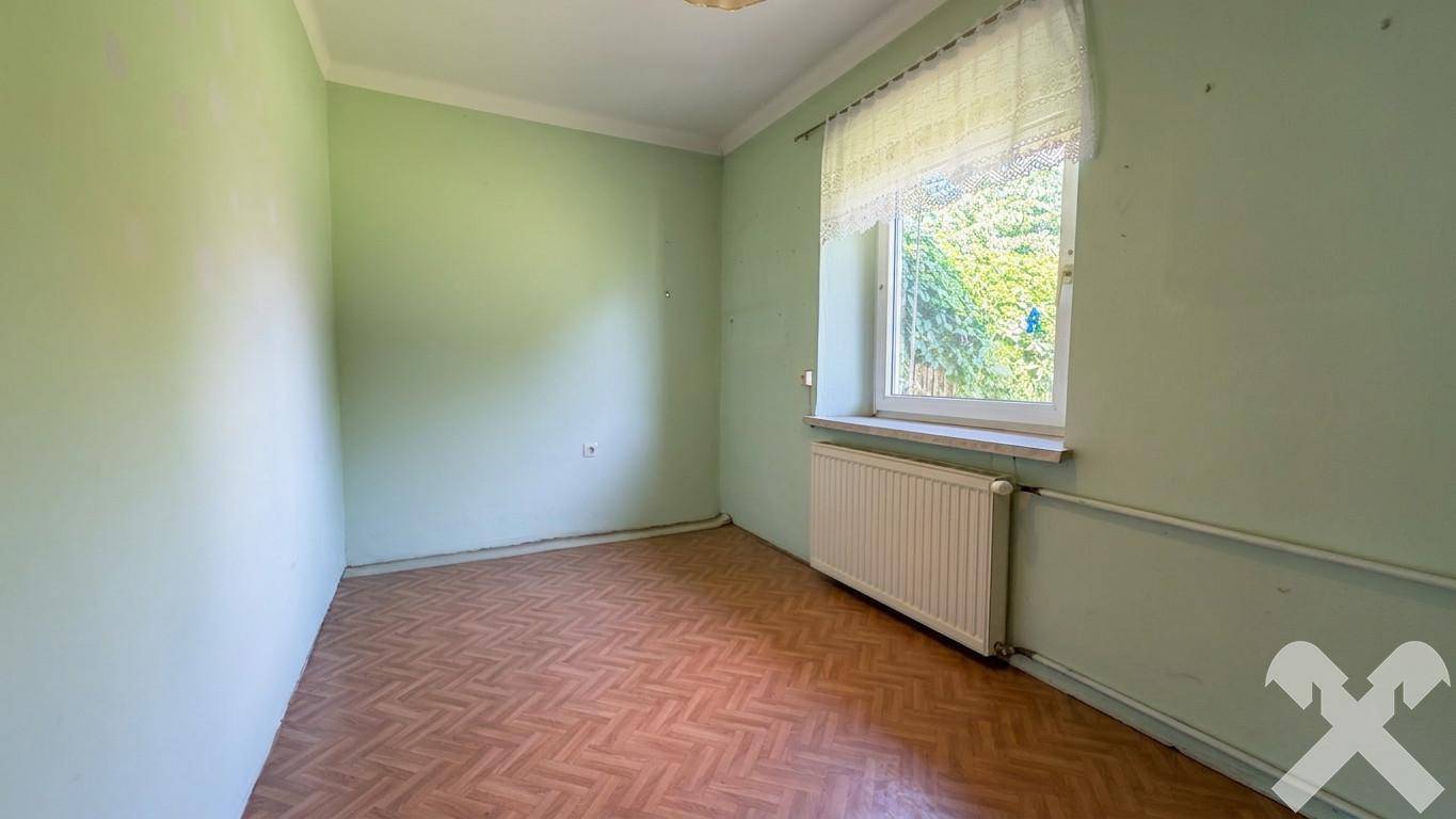Helles Zimmer mit grünen Wänden, Parkettboden und Fenster mit Blick ins Grüne.