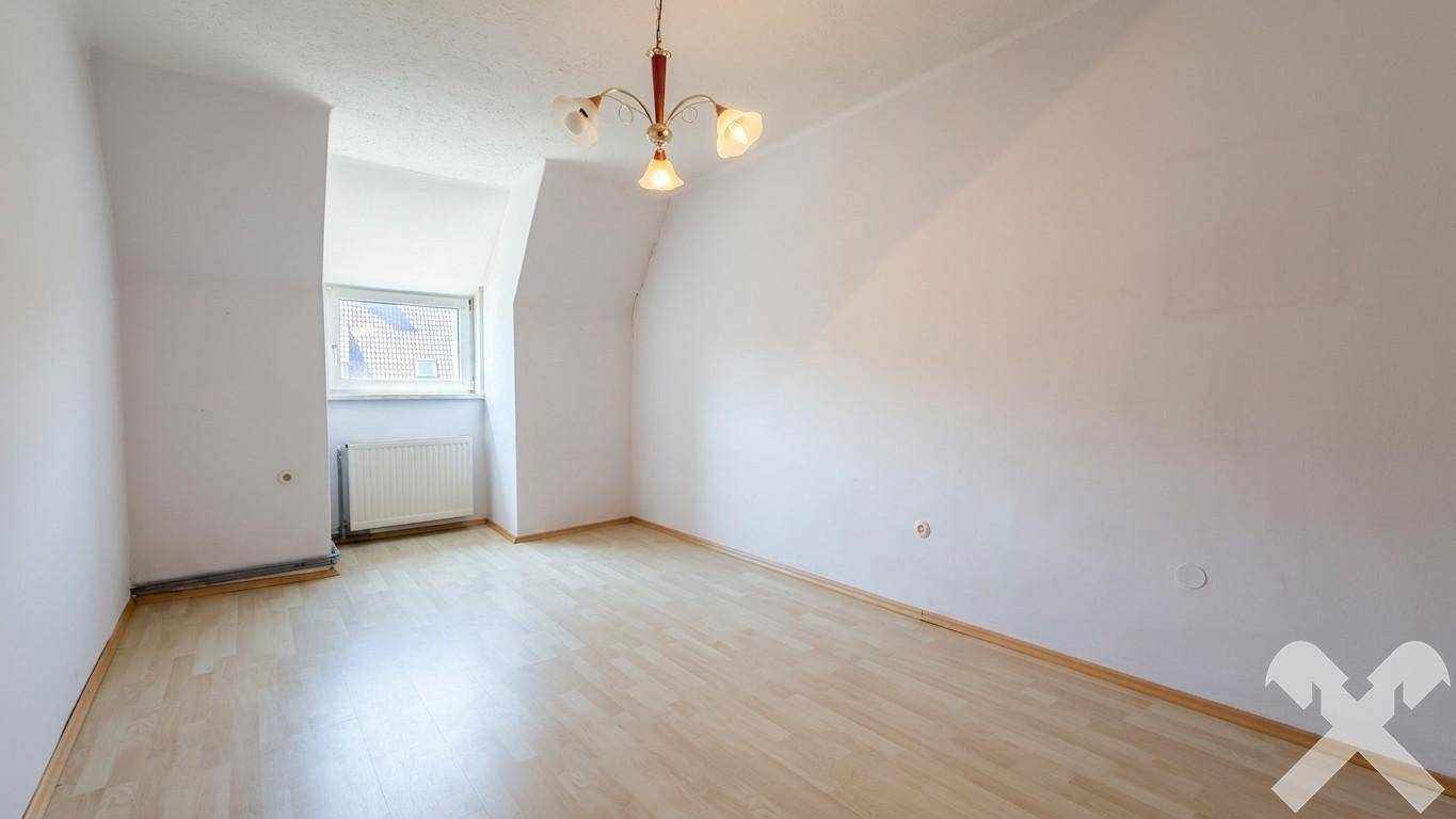 Helles, leeres Schlafzimmer im Dachgeschoss mit Dachschräge und Laminatboden.