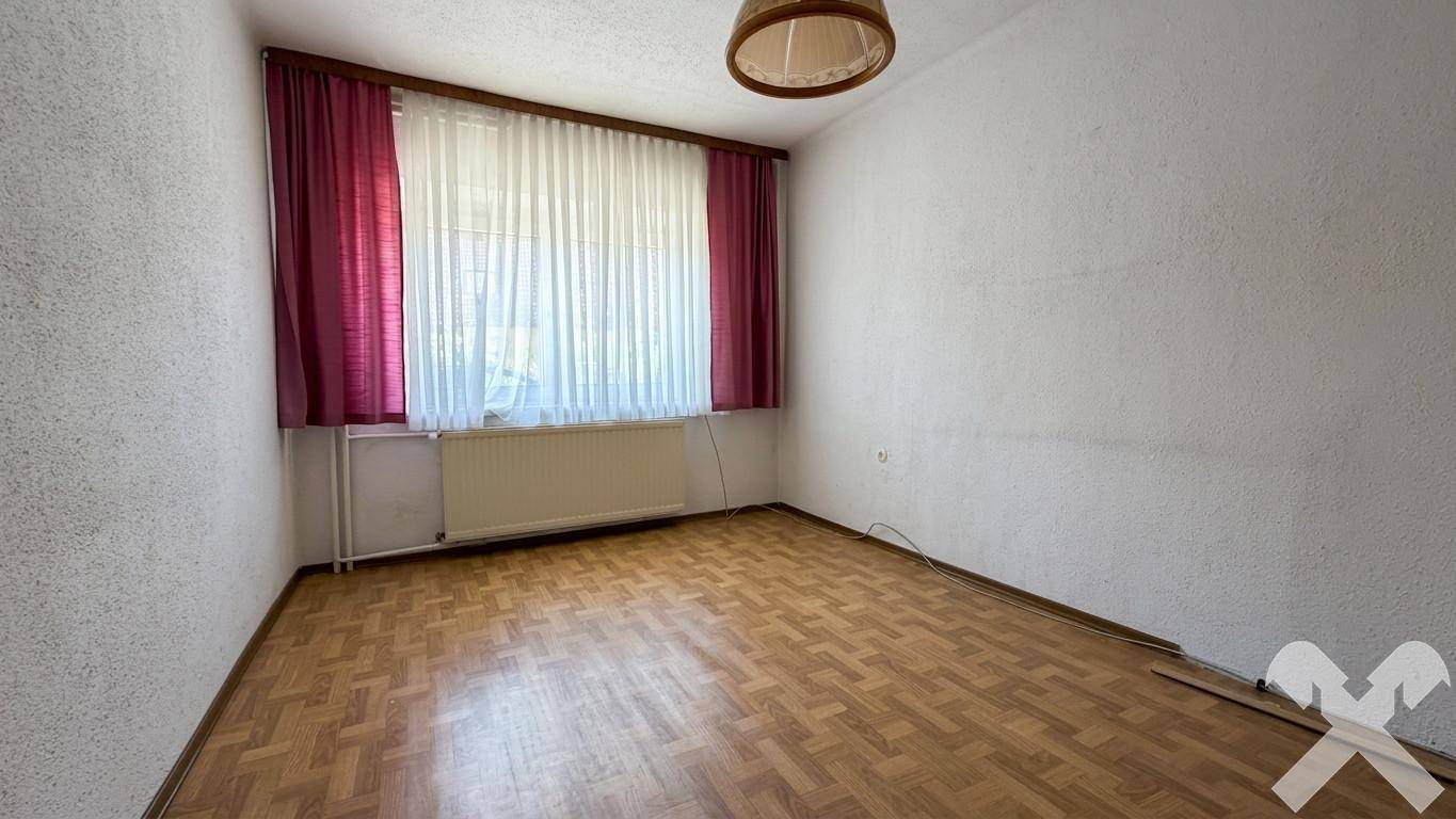 Geräumiges Zimmer mit Parkettboden, Fenster und roten Vorhängen, ideal als Schlafzimmer.