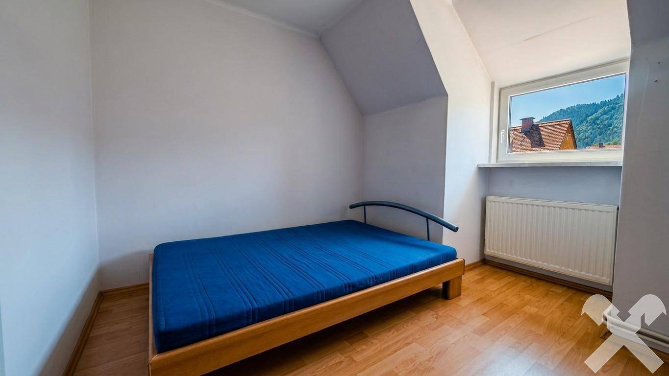 Schlafzimmer im Dachgeschoss mit Dachschräge, Holzbett und Fenster mit Bergblick.