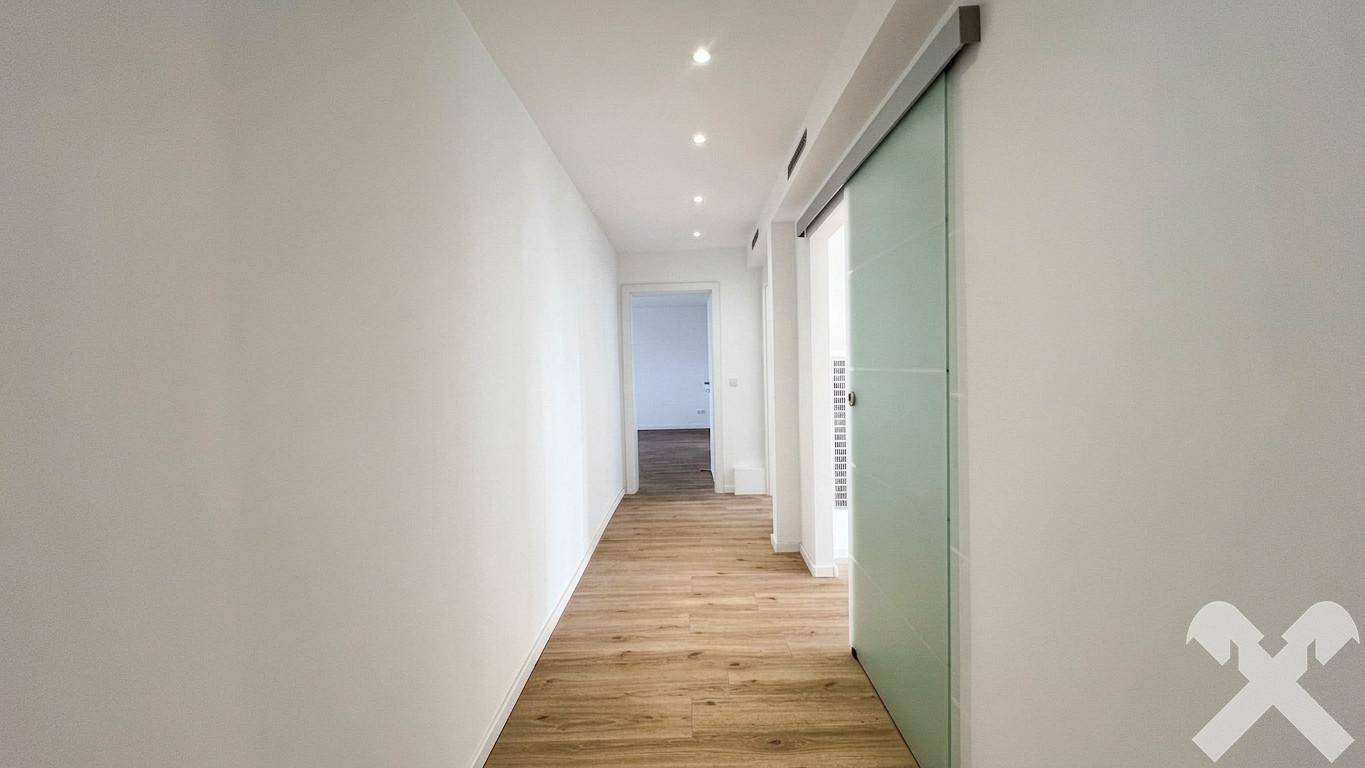Heller Flur mit modernem Laminatboden, weißen Wänden und einer eleganten Glasschiebetür.