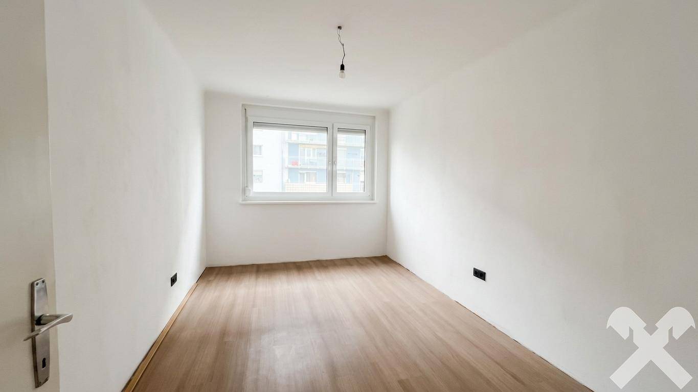 Unmöblierter Raum mit hellem Laminatboden, weißen Wänden und einem Fenster für Tageslicht.