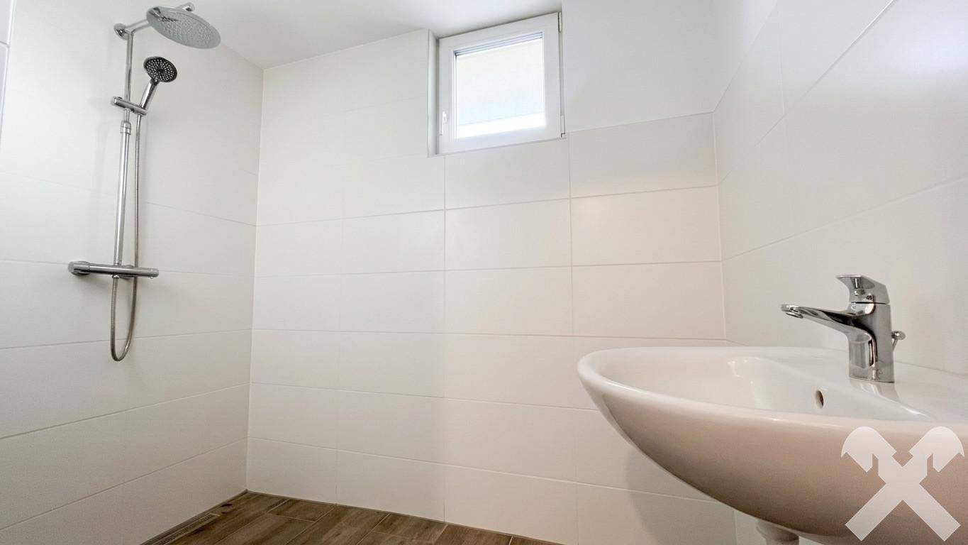 Modernes Badezimmer mit weißen Fliesen, Dusche, Einzelwaschbecken und kleinem Fenster.