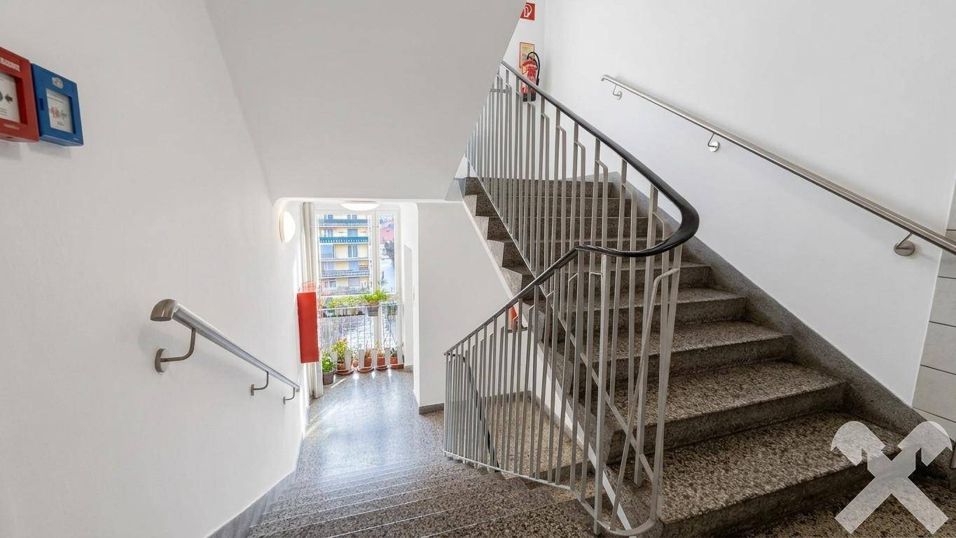 Helles Treppenhaus mit Granitstufen, Metallgeländer und Zugang zu einem kleinen Balkon.