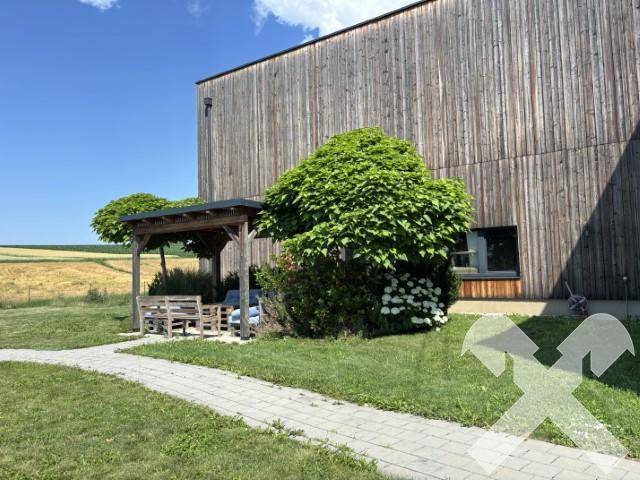 Ein kleiner Holzpavillon mit Sitzgelegenheiten im Grünen, umgeben von Bäumen und mit Blick auf die Felder.