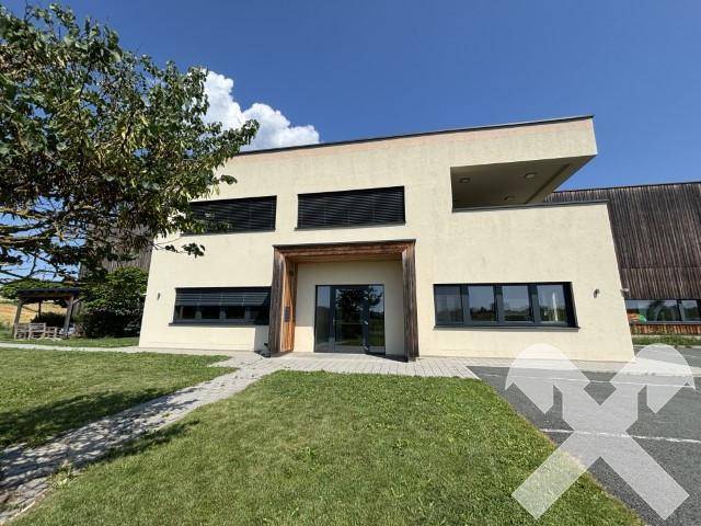 Vorderansicht des modernen Bürogebäudes mit beiger Fassade, dunklen Fenstern und Holzdetails am Eingangsbereich.