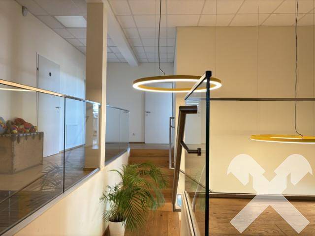 Blick auf eine moderne Treppe mit Holzstufen und Glasgeländer, beleuchtet von stilvollen runden Pendelleuchten.