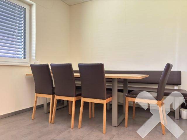 Essbereich in einer Küche oder einem Pausenraum mit Holztisch, Stühlen und einer Sitzbank am Fenster.
