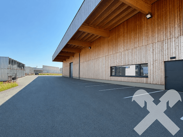 Außenansicht der großen Lagerhalle mit Holzfassade, breiter Zufahrt und sichtbaren Holzkonstruktionen unter dem Dachüberstand.