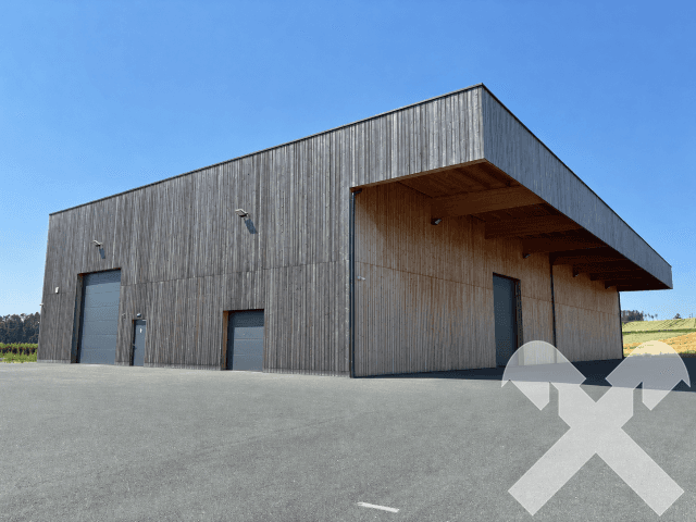Eckansicht der modernen Lagerhalle mit Holzfassade, mehreren Rolltoren und einer weitläufigen asphaltierten Fläche davor.