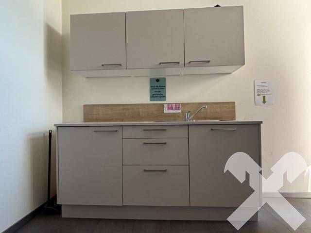 Kleine Küchenzeile mit grauen Schränken, Spüle und einer Holzrückwand, ideal für Pausen.