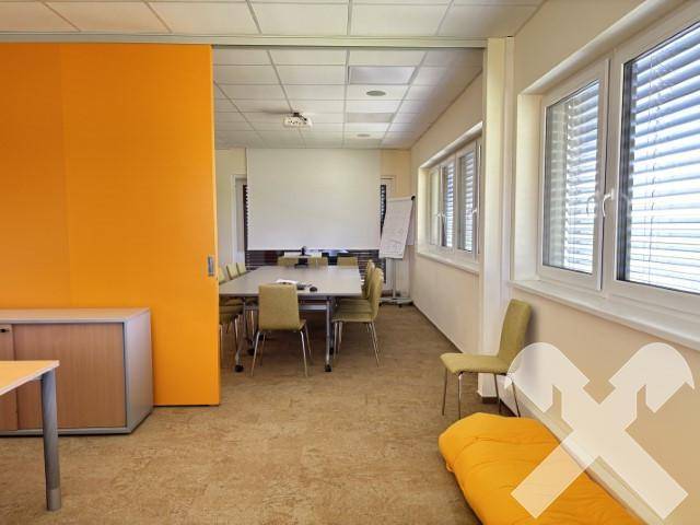 Konferenzraum mit flexibler Raumgestaltung durch eine verschiebbare orangefarbene Wand und Blick auf den Projektionsbereich.