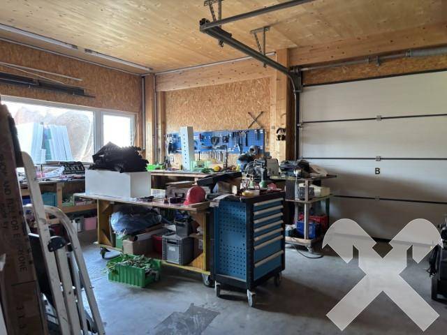 Werkstatt oder Garagenbereich mit Holzwänden und -decke, einer Werkbank voller Werkzeuge und einem großen Garagentor.
