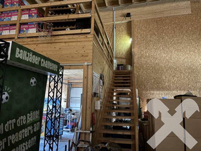 Geräumiger Lagerbereich mit Holzverkleidung, einer Holztreppe zur Empore und verschiedenen Lagergütern.
