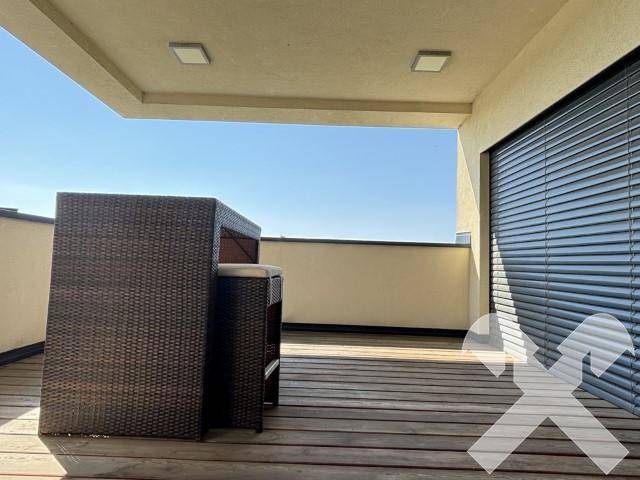 Nahaufnahme der Loggia mit Holzdeck und modernen Rattan-Gartenmöbeln unter blauem Himmel.
